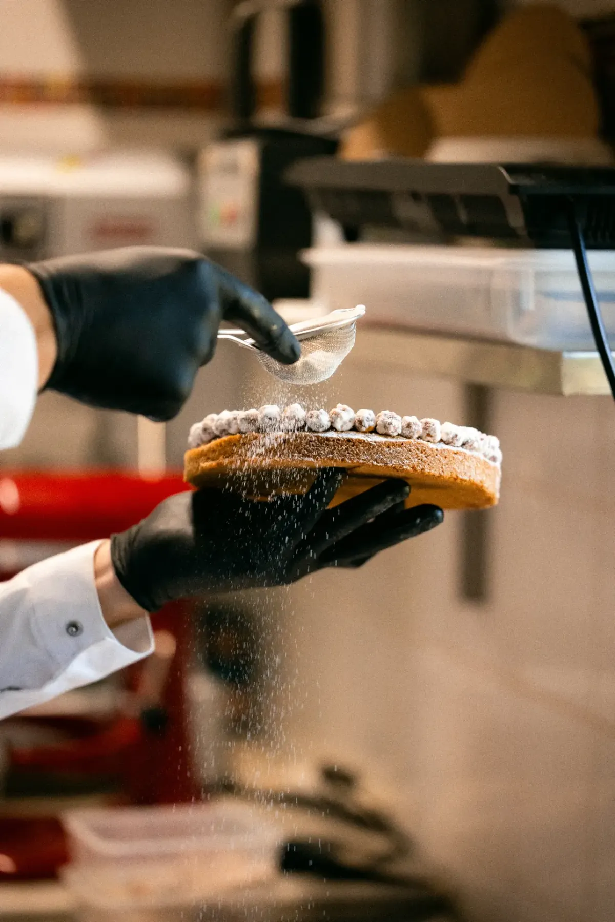 Mains gantées saupoudrant de sucre glace un entremets végétal à l'aide d'un tamis © Leslie Leyzour
